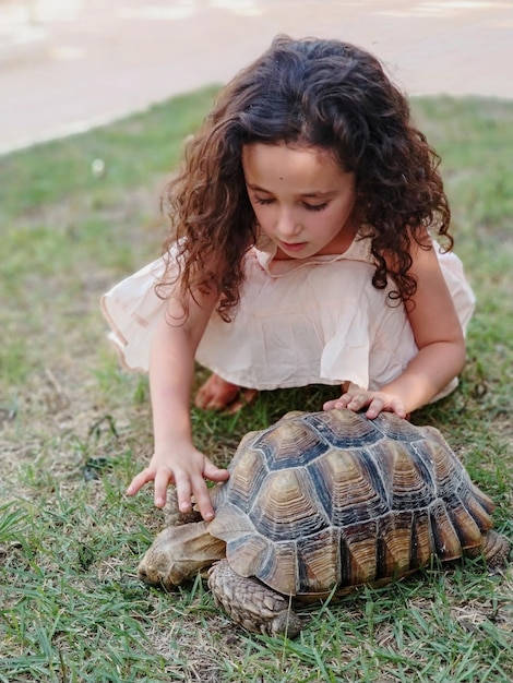 Foto meisje die een schildpad aanraakt terwijl ze op het veld kruipt