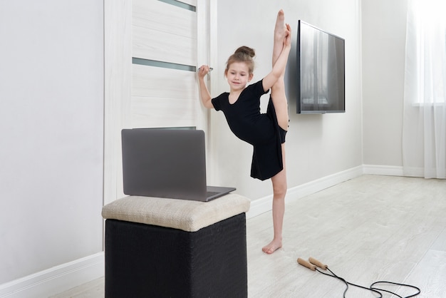 Meisje die gymnastiekoefeningen doen die thuis het online leren met laptop computer gebruiken