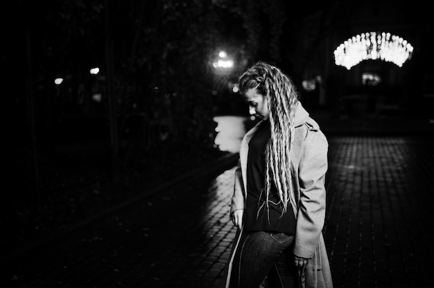 Meisje die met dreadlocks bij nachtstraat van stad tegen slingerlichten lopen.