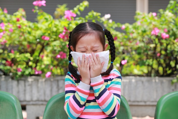 Meisje die op neus met papieren zakdoekje niezen terwijl openlucht