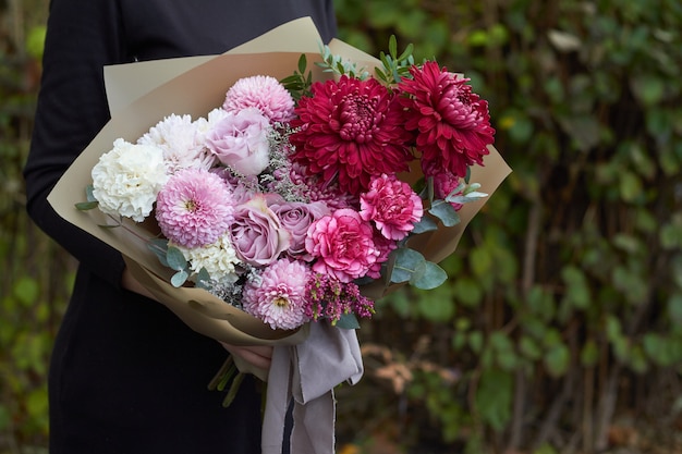 Meisje die roze en purper gestemd boeket in uitstekende stijl in openlucht tegenover het park houden