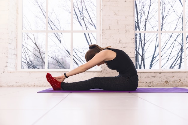 Meisje doet een asana naar voren buigen met haar handen naar haar benen. Op de vloer zitten