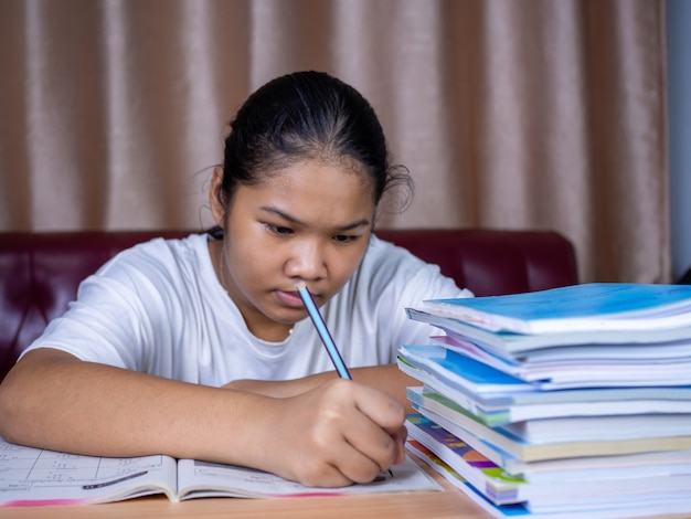 Meisje doet huiswerk op een houten tafel en er was een stapel boeken ernaast. De achtergrond is een rode bank en crèmekleurige gordijnen.