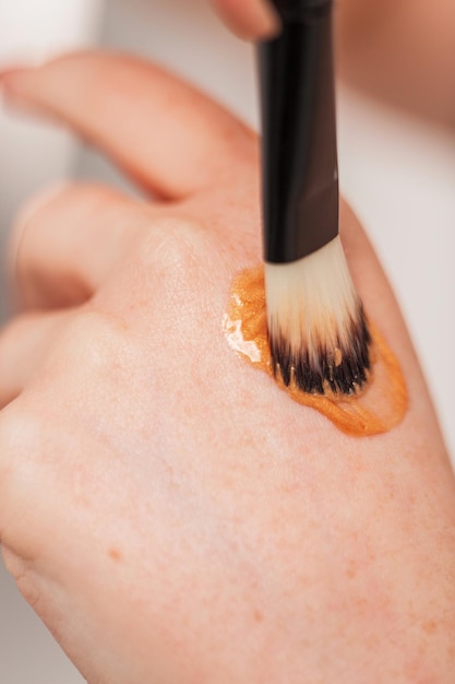 Meisje doet make-up met markeerstift crème op haar hand en een borstel close-up Schoonheid en huidverzorging