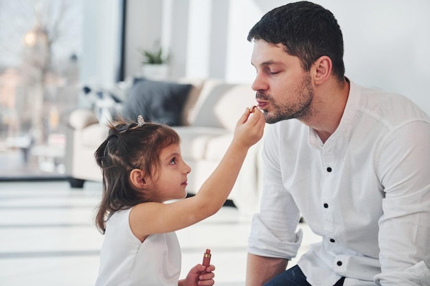 Meisje doet make-up voor papa Gelukkige vader met zijn dochter die samen vrije tijd thuis doorbrengt