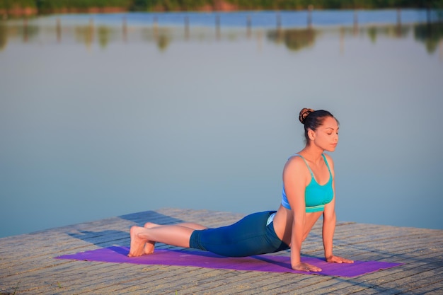 Meisje doet yoga op de oever bij zonsondergang.