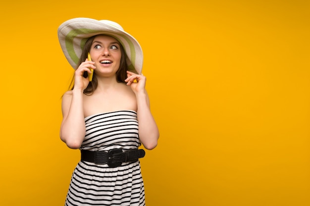 Meisje draagt strooien hoed en korte witte stroken jurk met open schouders praten over een smartphone
