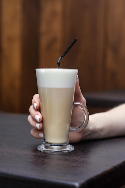 Foto meisje drinkt koffie in een glas met een rietje en schuim in een koffiewinkel