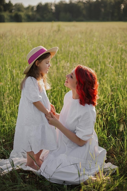 Meisje een kind met een hoed knuffel moeder vrouw met rood haar zitten op een groen veld bij zonsondergang