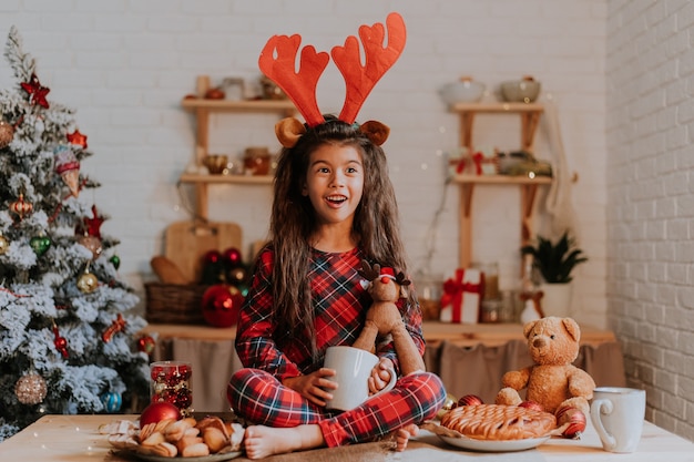 Meisje eet een kersttaart en drinkt thee uit een witte mok in een prachtig ingerichte keuken