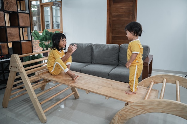 meisje en haar kleine zusje zitten op het bord terwijl ze samen spelen in het speelgoed van de pikler-driehoek