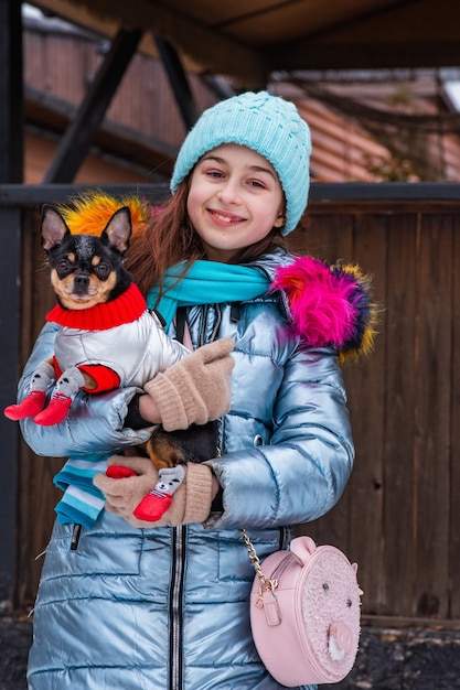 Meisje en hond in de winter. meisje in blauw jasje. Hond in kleren. Tiener lachend met een huisdier in haar armen