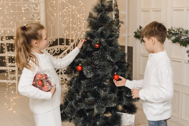 Meisje en jongen, broer en zus hangen nieuwjaarsspeelgoed aan de takken van sparren. Familie Kerstmis en Nieuwjaar concept