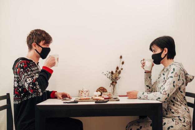 Meisje en jongen ontbijten thuis in maskers.