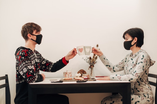 Foto meisje en jongen op quarantaine koffie drinken in maskers.