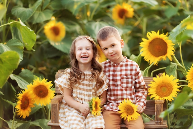 meisje en jongen zitten op een bankje en hebben plezier tussen bloeiende zonnebloemen bij zonsondergang