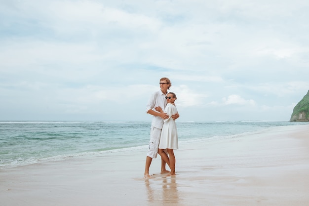 Meisje en man in witte kleren op een wit strand en knuffelen