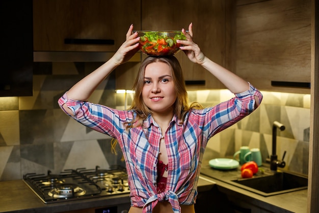 Meisje fitness trainer vegetarische voedingsdeskundige bereiden verse groentesalade in de keuken. Kijken naar haar figuur