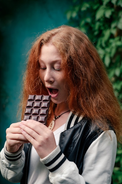 Foto meisje gaat zoete chocoladereep eten. tiener met rood haar houdt van snoep