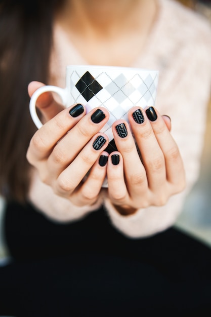 Meisje handen met een kopje koffie met mooie zwarte manicure.