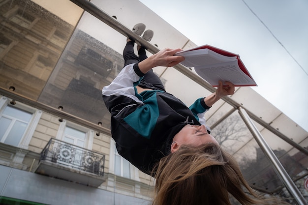 Meisje hangt aan de voeten ondersteboven in de straat en leest boekconcept van onderwijs en zelfontwikkeling...