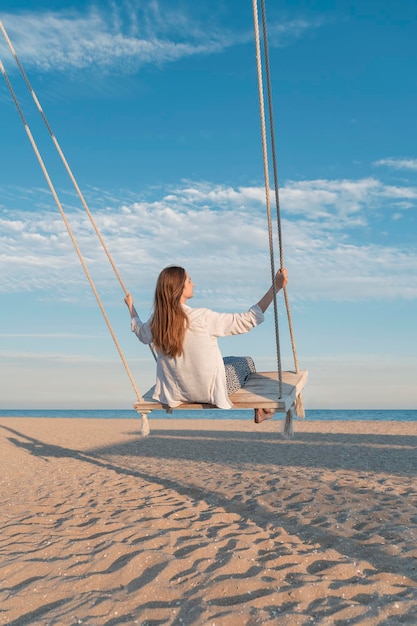 Meisje heb plezier swingend hoog in de lucht jonge vrouw in wit shirt op touw swingend op blauwe lucht en zee achtergrond