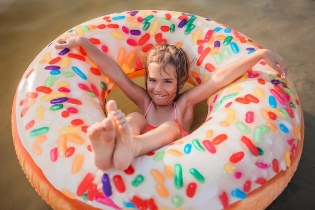 Meisje heeft plezier op de opblaasbare ring van de grote donut op het meer op hete zomerdag, gelukkig zomers platteland