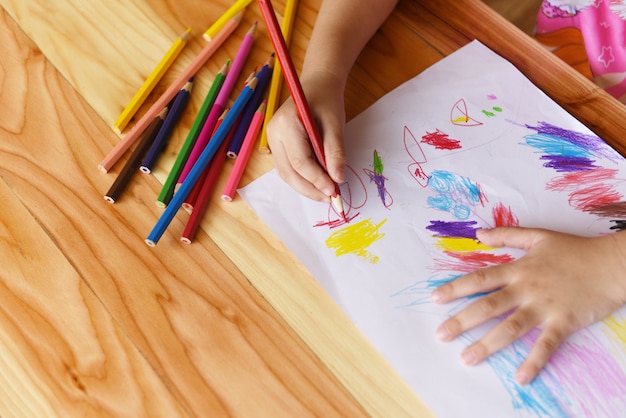 Meisje het schilderen op document blad met kleurenpotloden op de houten lijst thuis - kindjong geitje die tekeningsbeeld en kleurrijk kleurpotlood doen