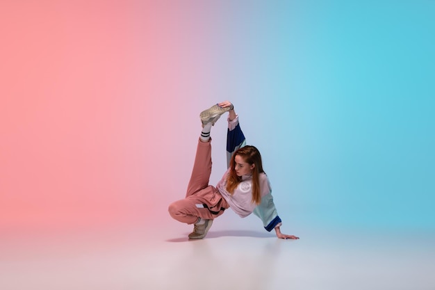 Meisje hiphop dansen in stijlvolle kleding op achtergrond met kleurovergang in danszaal in neonlicht