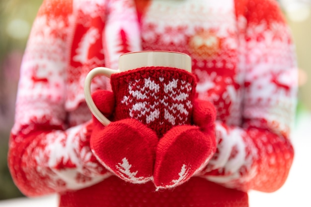 Meisje houdt de beker glühwein in handen buiten in de winter. Vrouw draagt trui en handschoenen met kerstversiering. Kerst vakantie concept