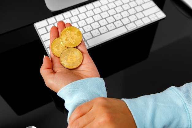Foto meisje houdt een crypte in bitcoin zijn hand op de achtergrond van een laptop
