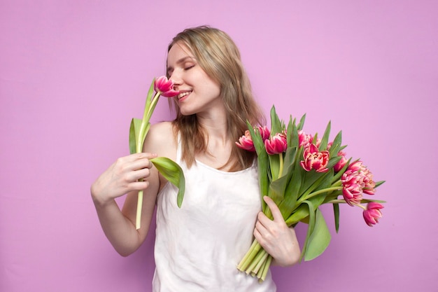 Meisje houdt en snuift een boeket bloemen op een roze achtergrond een mooie vrouw met tulpen