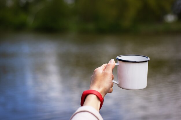 meisje houdt in haar handen een metalen kopje koffie in de buurt van het meer.