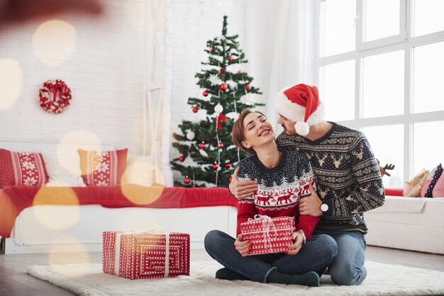 Meisje houdt kerstcadeau van haar man in de buurt van het decoratieve bed en de boom.