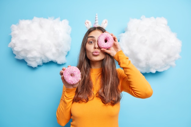 Foto meisje houdt lippen gevouwen houdt geglazuurde donut tegen oog met zoet dessert eet graag junkfood dat veel calorieën bevat