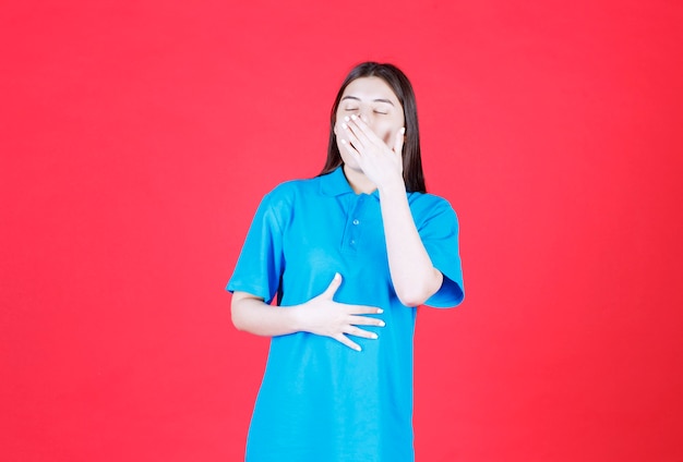 Meisje in blauw shirt dat op de rode muur staat en adem inhoudt vanwege de slechte geur.