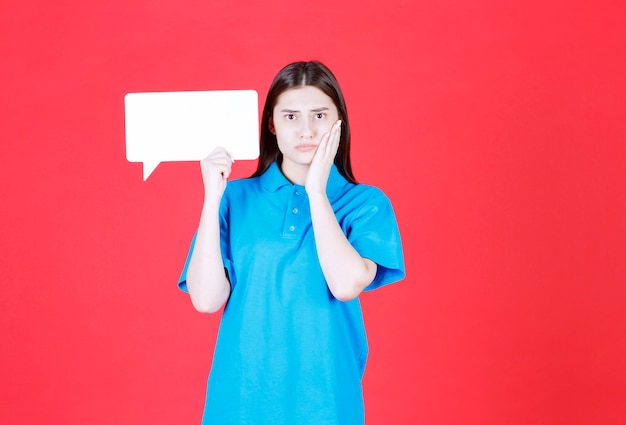 Meisje in blauw shirt met een rechthoekig infobord en ziet er verward en attent uit