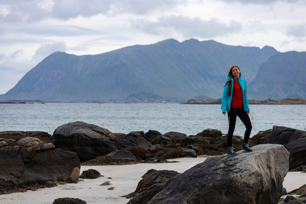 meisje in blauwe jas loopt op het strand met enorme rotsen en bergen op de achtergrond, Lofoten