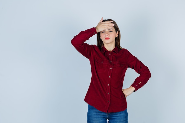 meisje in bordeauxrode blouse die hand op het voorhoofd houdt en er gestrest uitziet