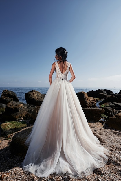 Meisje in bruiloft luxe jurk poseren op zee. Bruid op rotsen.