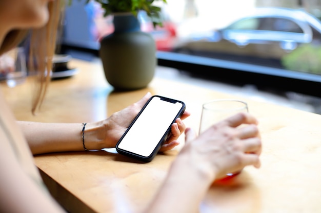 Meisje in café aan tafel heeft een telefoon met een leeg scherm in haar hand. plaats voor uw ontwerp