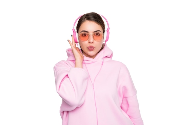 Meisje in casual roze hoodie en bril luisteren naar muziek in koptelefoon pruilende lippen geïsoleerd op wit