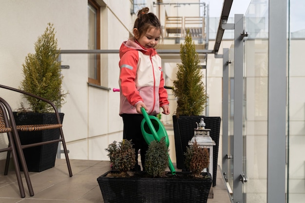 Foto meisje in de kleuterschool water planten op het balkon in het voorjaar balkon stedelijke tuin