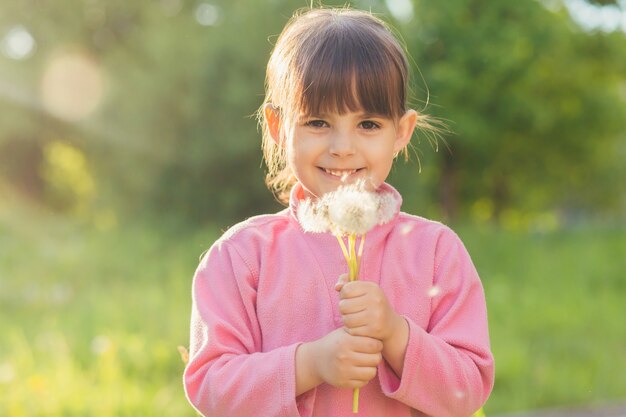 meisje in de natuur verzamelt snuifjes en blaast op paardebloemen