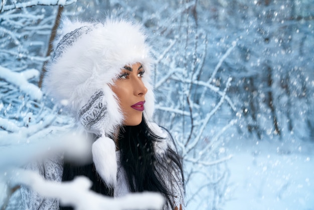 Meisje in de winter witte hoed in bos met sneeuw dichtbij bomen.