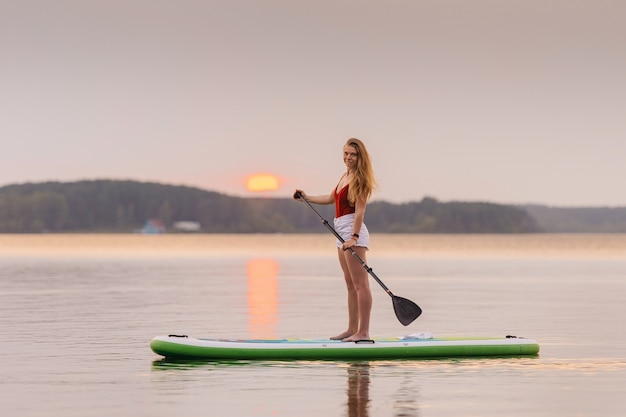 Meisje in de zee opstaan op de peddel sup board met prachtige zonsondergang of zonsopgang waterkleuren.