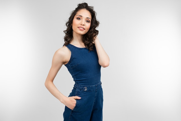 Meisje in de zomer blauwe overall die op een grijze achtergrond met exemplaarruimte stellen