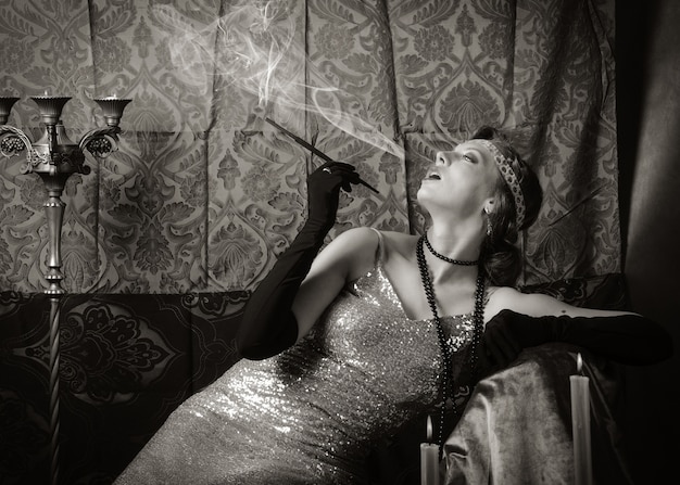 Foto meisje in een avondjurk met een sigaret mondstuk. studioportret in retrostijl, afgezwakt in sepia