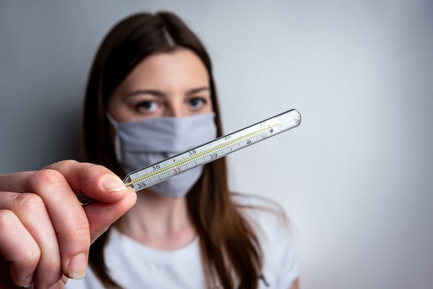 Meisje in een beschermend gezichtsmasker met een thermometer in haar hand. Coronavirus (COVID-19.