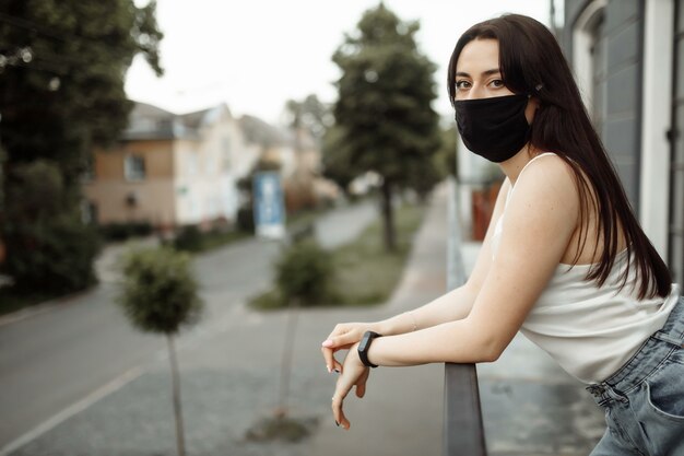 Meisje in een beschermend masker op een balkon kijkt naar een lege stad